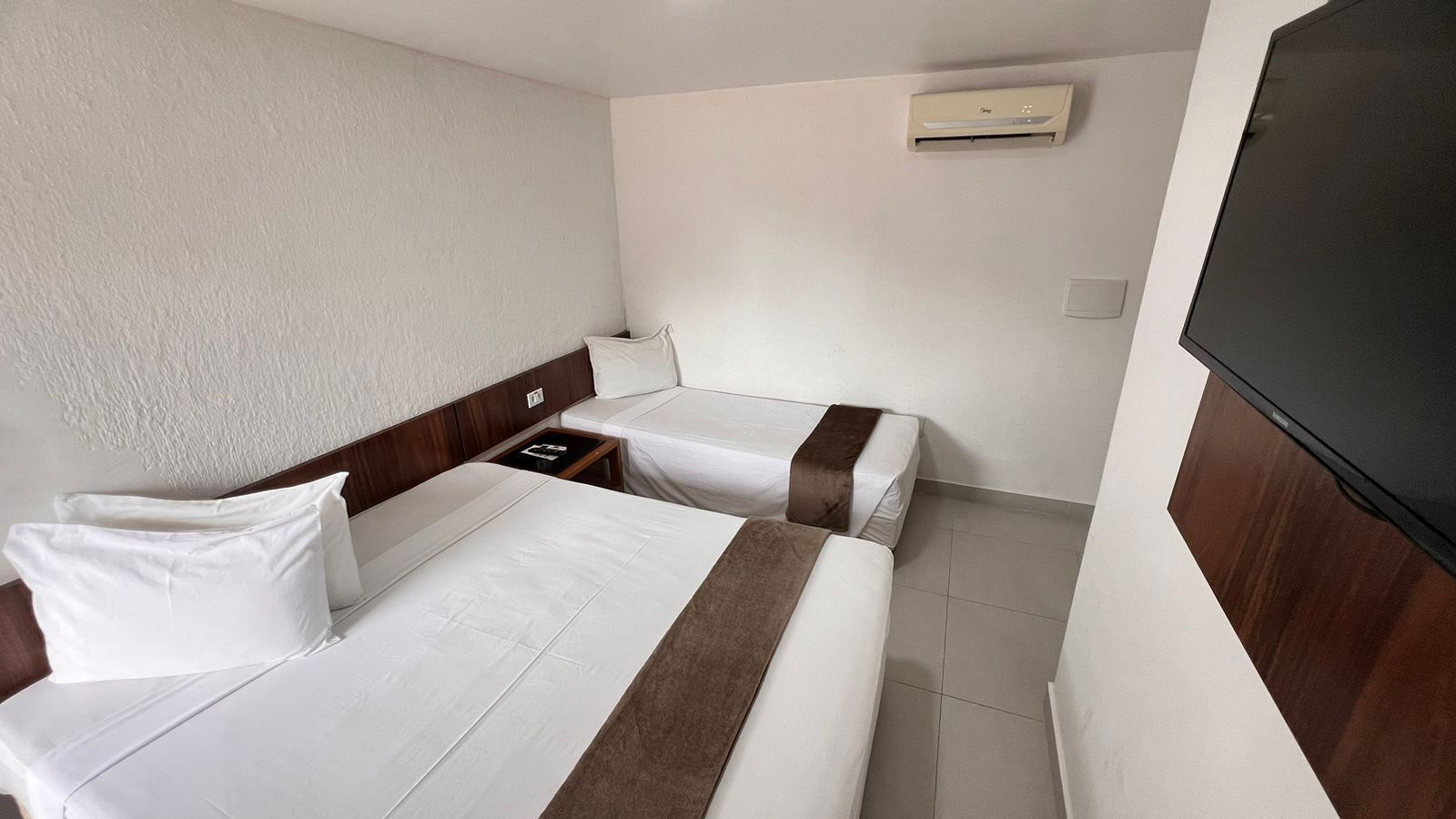 A hotel room with two beds, a TV, and a wall-mounted air conditioner.