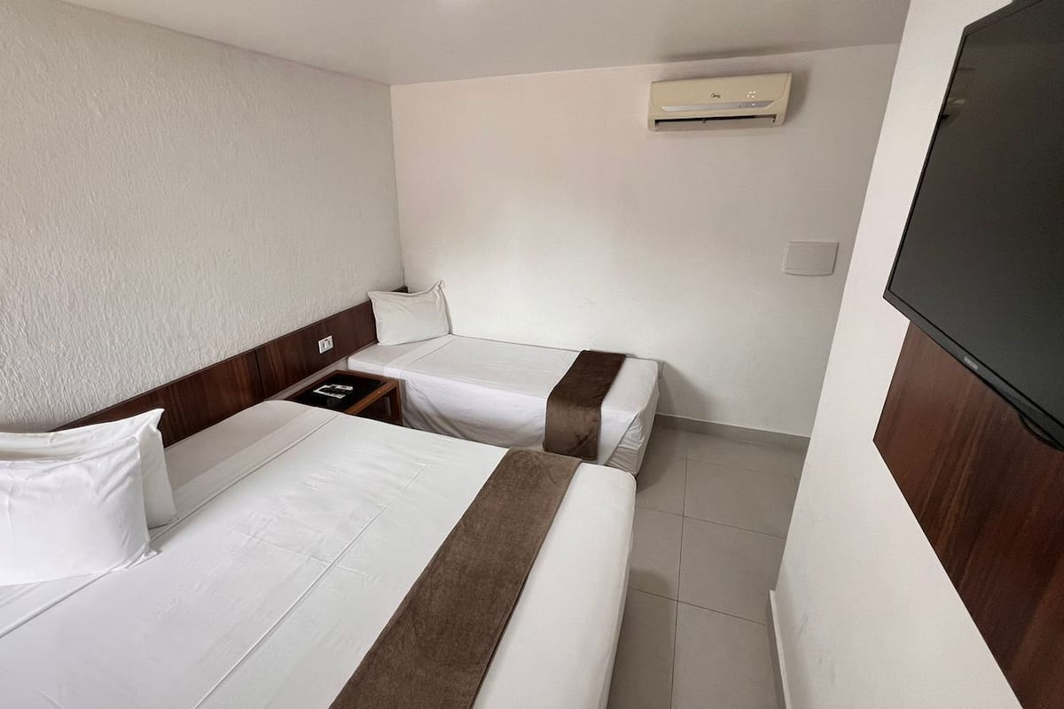 A hotel room with two beds, a TV, and a wall-mounted air conditioner.