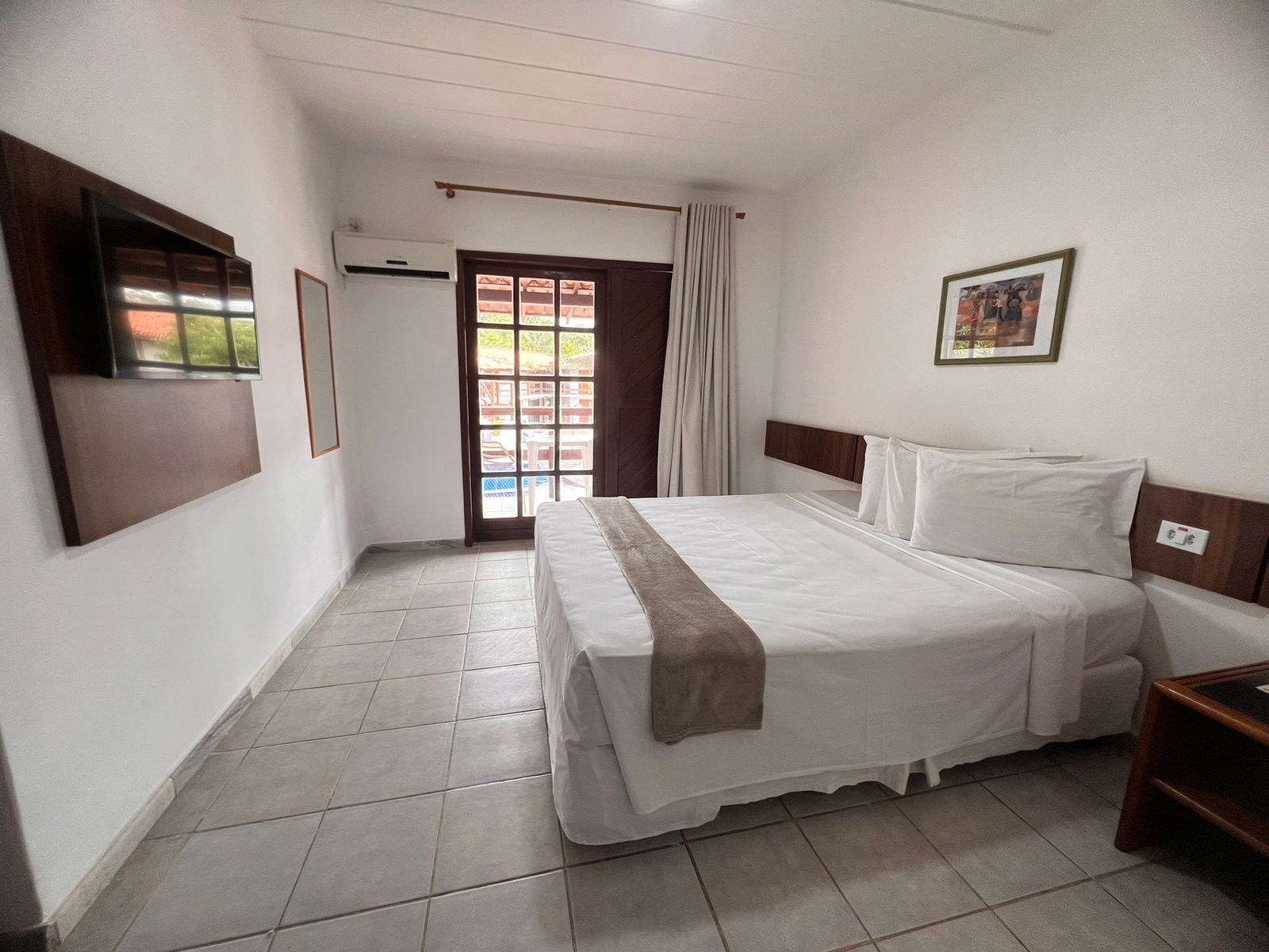 A hotel room with a bed, a TV, a window, and a door.