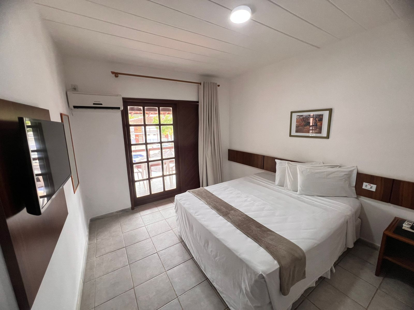 A hotel room with a bed, a TV, a window, and a door.
