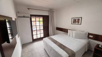 A hotel room with a bed, a TV, a window, and a door.