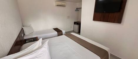 Habitación de hotel con dos camas individuales, un televisor montado en la pared, un escritorio pequeño y un refrigerador minibar.