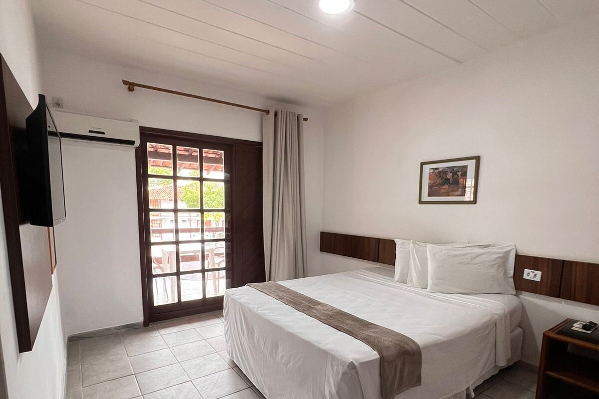 Une chambre d’hôtel avec un lit, une télévision, une fenêtre avec des rideaux et un tableau au mur.