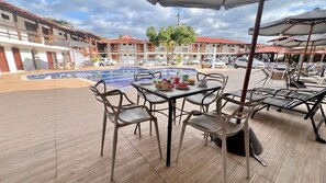 Un espace aménagé au bord de la piscine, avec une table et des chaises, une piscine, et des bâtiments en arrière-plan.