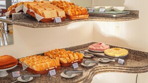 A buffet with various bread and pastries, including a cake, arranged on granite countertops. - Rede Andrade Estrela Dalva Praia (Porto Seguro)