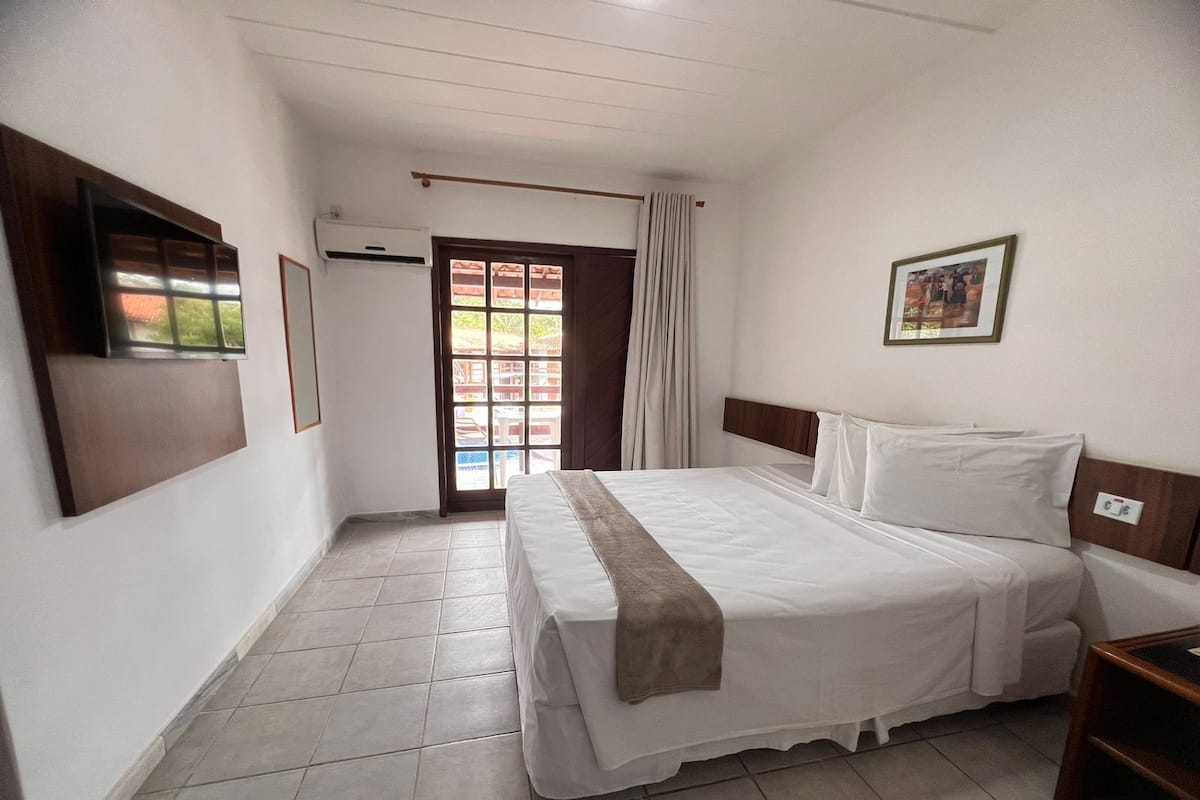 A hotel room with a bed, a TV, a window, and a door.