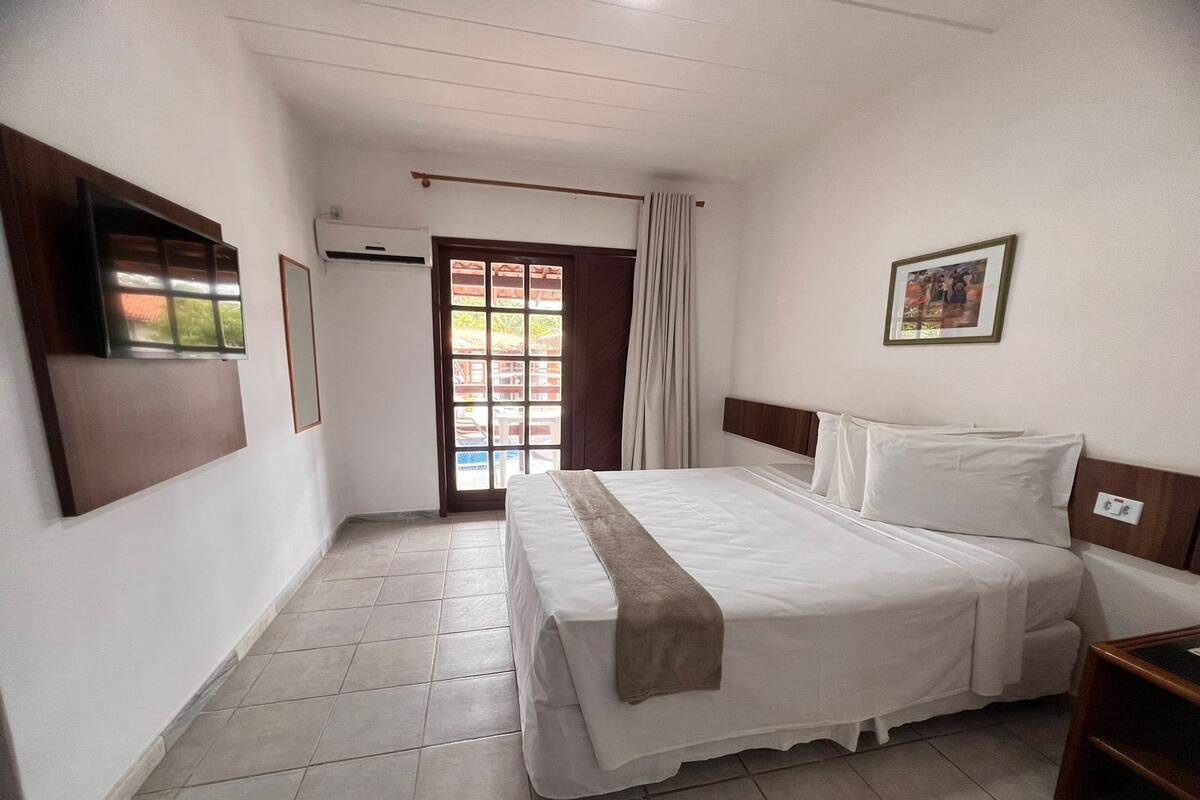 A hotel room with a bed, a TV, a window, and a door.