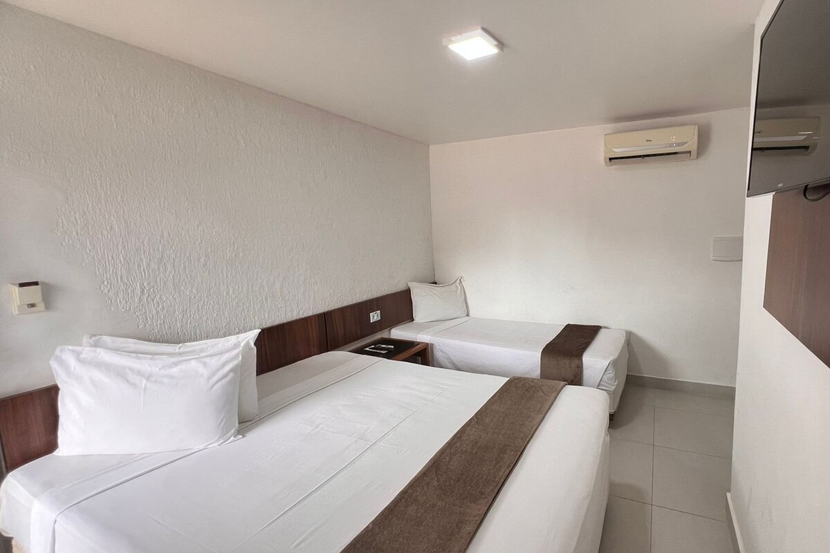 Une chambre d’hôtel avec deux lits, une tête de lit en bois, une table de chevet, un climatiseur mural et un téléviseur.