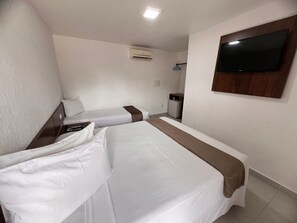 Quarto de hotel com duas camas de solteiro, televisão fixada na parede, ar condicionado e uma pequena escrivaninha com cadeira.