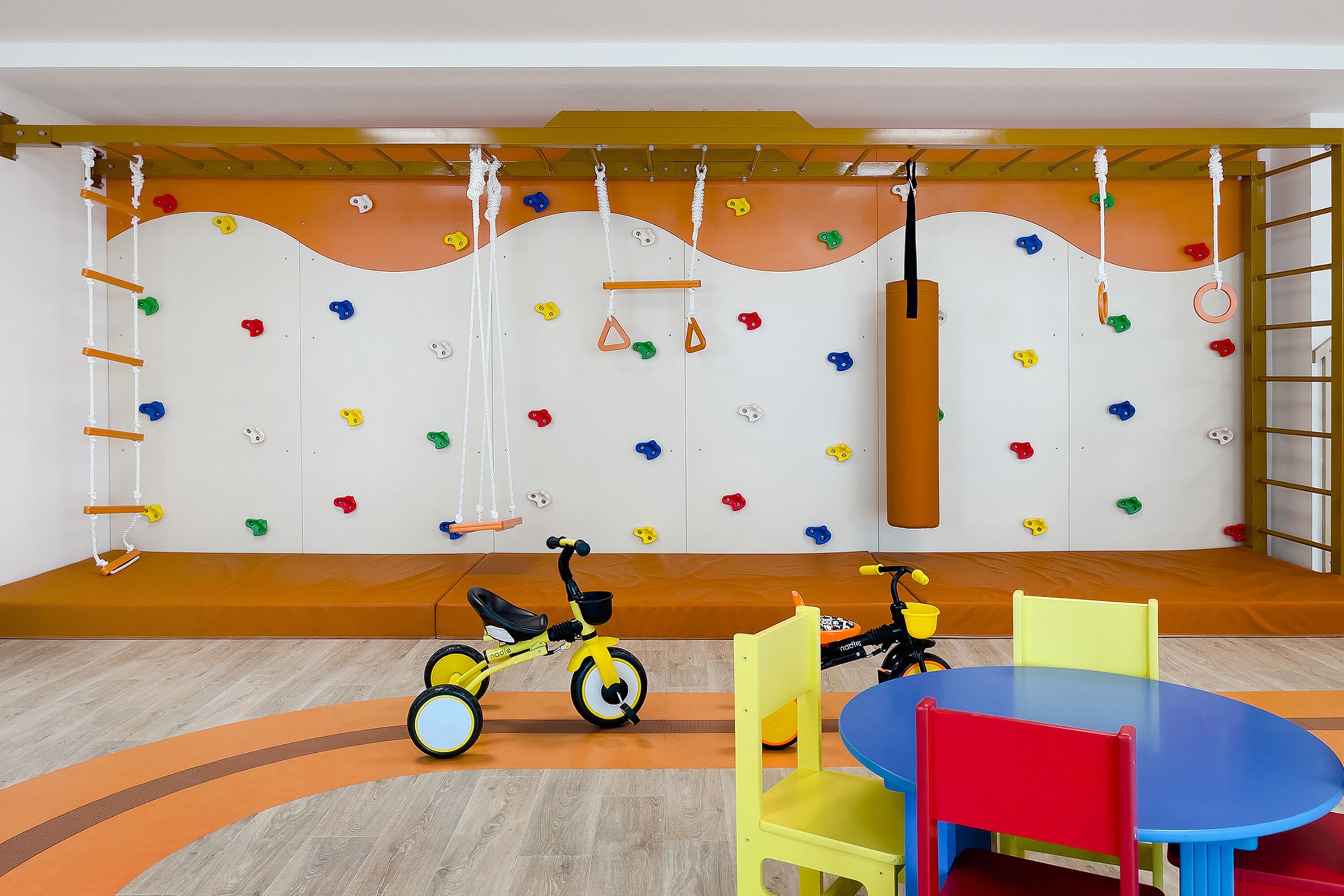 A children's play area with a climbing wall, two tricycles, and a table with chairs.