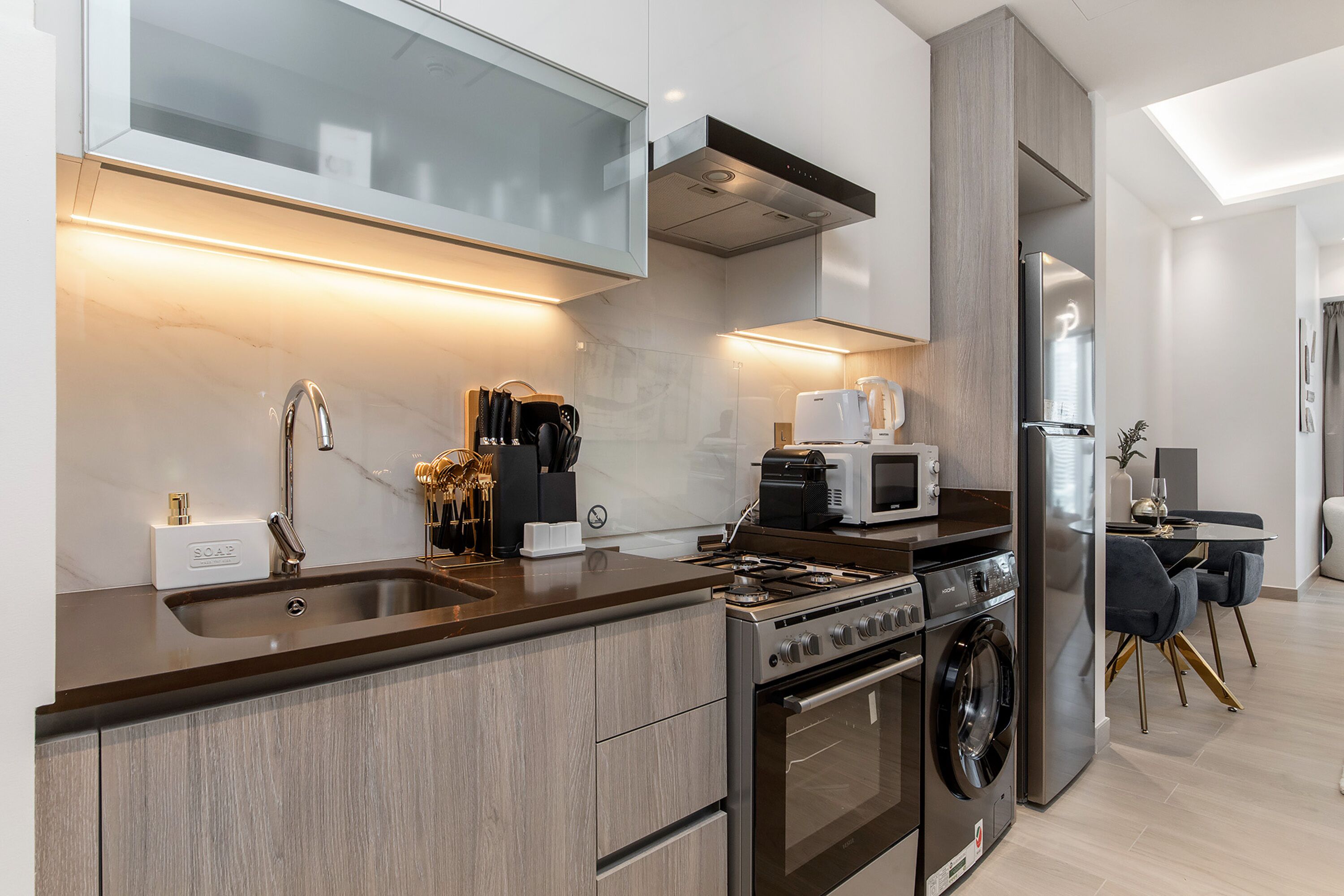 Una cocina moderna con un lavaplatos de acero inoxidable, horno empotrado, microondas y lavavajillas.