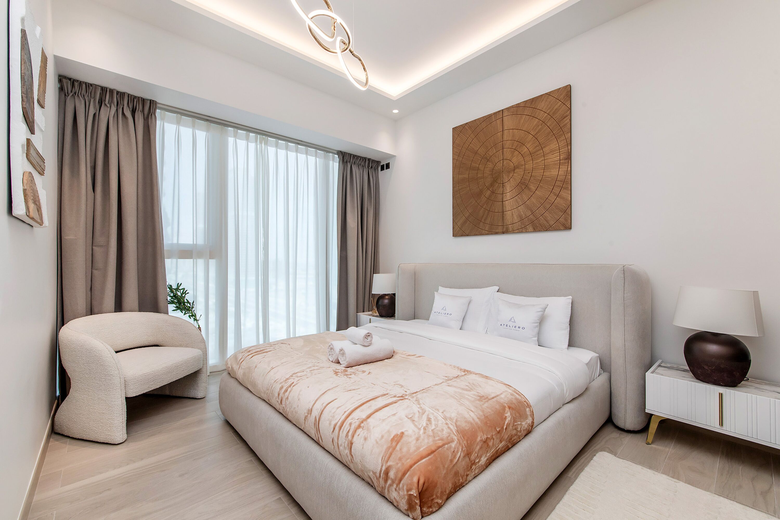 A modern bedroom with a large bed, a curved armchair, and a nightstand with lamps.