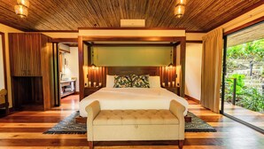 A spacious bedroom with a large bed, a bench, and a view of a garden. - Secret Bungalows Lechu (Penas Blancas)