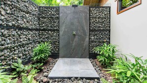 A modern outdoor shower area with a stone wall, surrounded by tropical plants. - Secret Bungalows Lechu (Penas Blancas)