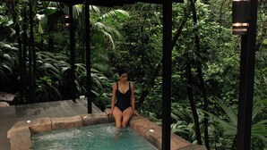 A woman in a black swimsuit sitting in a small pool surrounded by lush greenery. - Secret Bungalows Lechu (Penas Blancas)