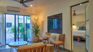 A modern hotel room with a large bed, a TV, a dining area with a table and chairs, a ceiling fan, and a view of the outdoors. - Casa Azalea in Garcia Ginerés near Downtown (Merida)