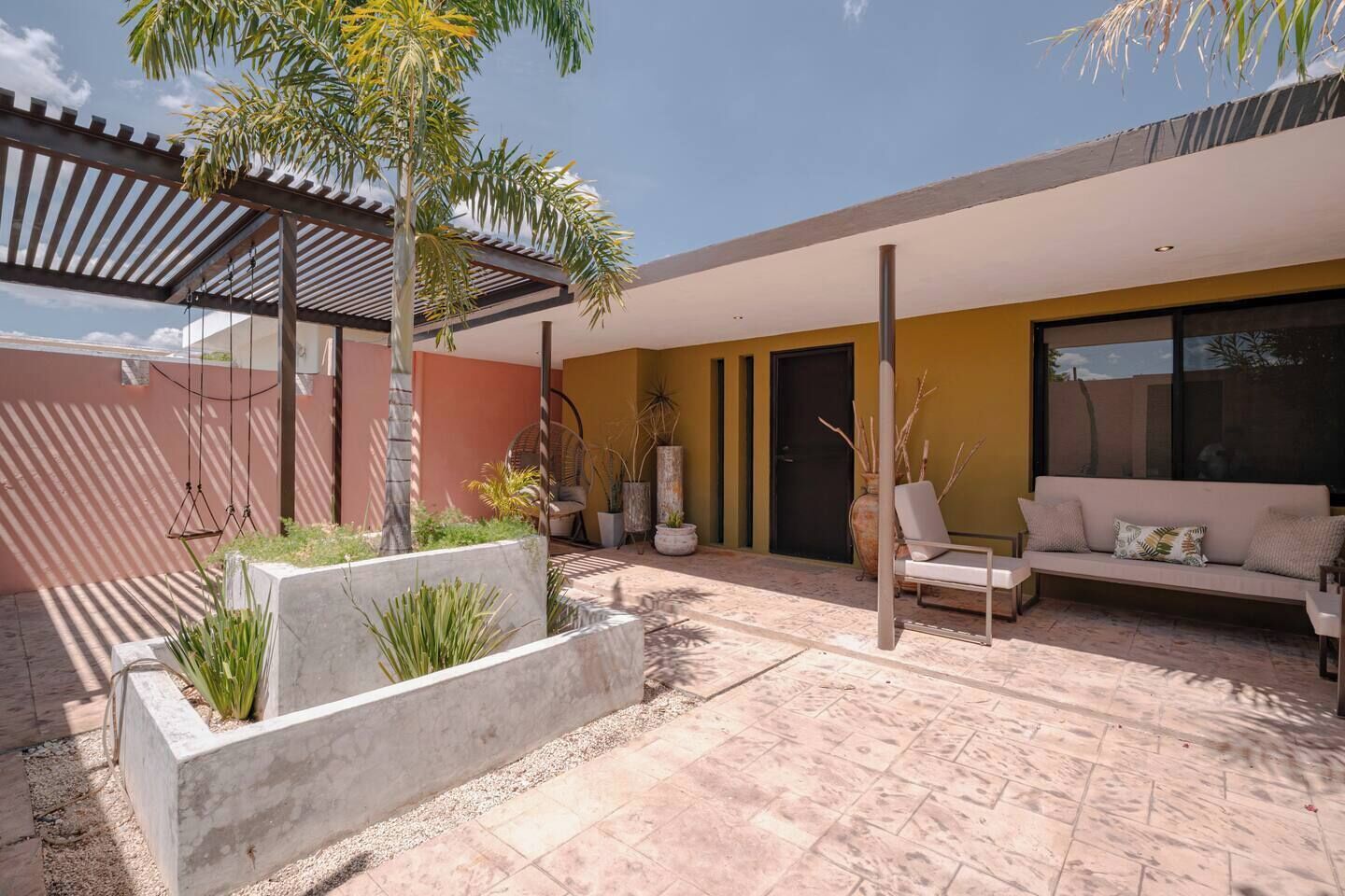 A modern outdoor patio with a seating area, a pergola, and a variety of plants.