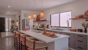 A modern kitchen with a central island, bar stools, hanging wicker lights, and a large window. - Casa Azalea in Garcia Ginerés near Downtown (Merida)
