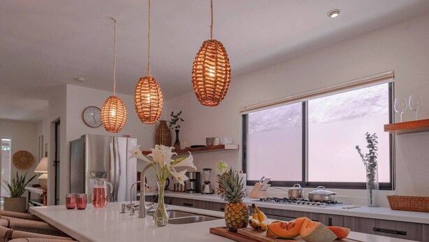 A modern kitchen with a large island, wicker pendant lights, and a view of the outdoors through a large window. - Casa Azalea in Garcia Ginerés near Downtown (Merida)