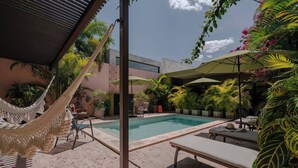 Zona de piscina con hamaca, sillas de descanso y plantas en macetas.