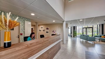 Una zona de recepción moderna con un mostrador de madera, un jarrón grande con plumas de pampa y un área de estar con sofá y sillones.