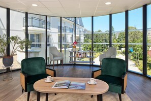 Una habitación moderna con ventanas amplias, dos sillas verdes, una mesa de madera y una estantería.