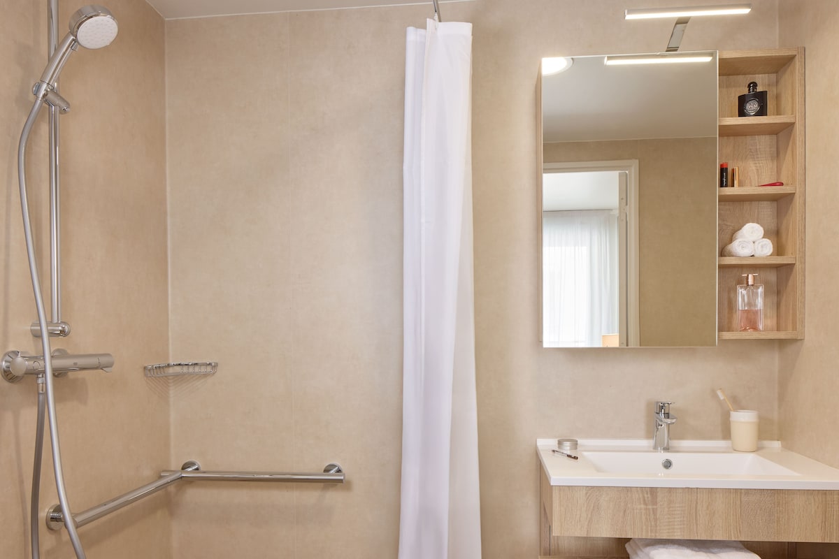 Un baño con ducha, lavamanos, espejo y un estante con artículos de aseo.