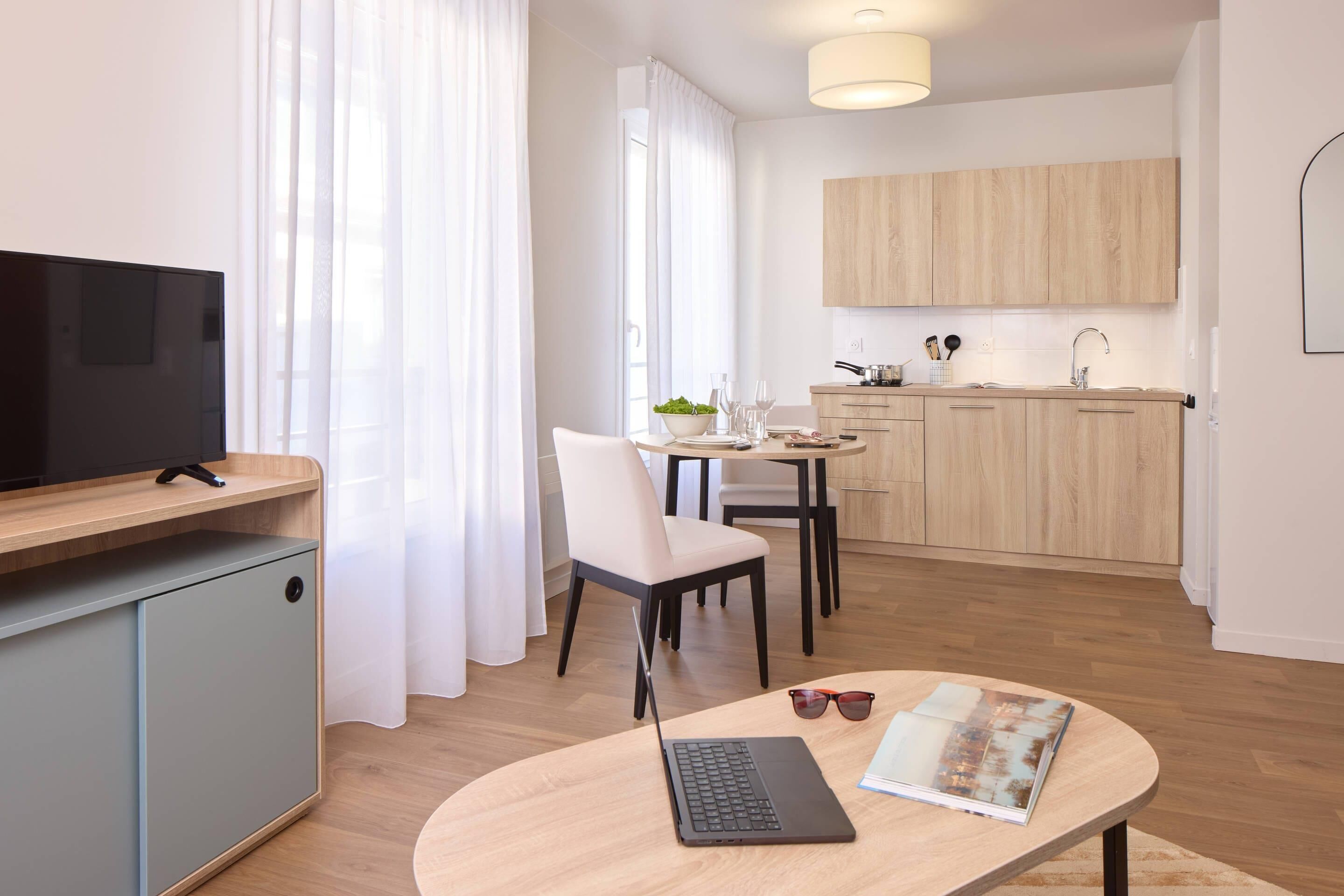 Una habitación de hotel moderna con una televisión de pantalla plana, una computadora portátil y un área de comedor con una mesa y sillas.