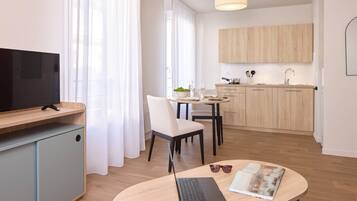 Una habitación de hotel moderna con una televisión de pantalla plana, una computadora portátil y un área de comedor con una mesa y sillas.