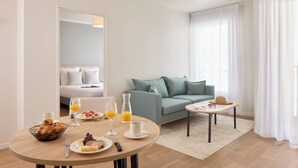 Una habitación de hotel moderna con una mesa redonda para el desayuno, un sofá y una mesita auxiliar con un sombrero.