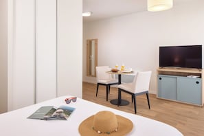 A modern hotel room with a dining area, a TV, and a bookshelf. - Quality Aparthotel Cherbourg (Cherbourg-en-Cotentin)