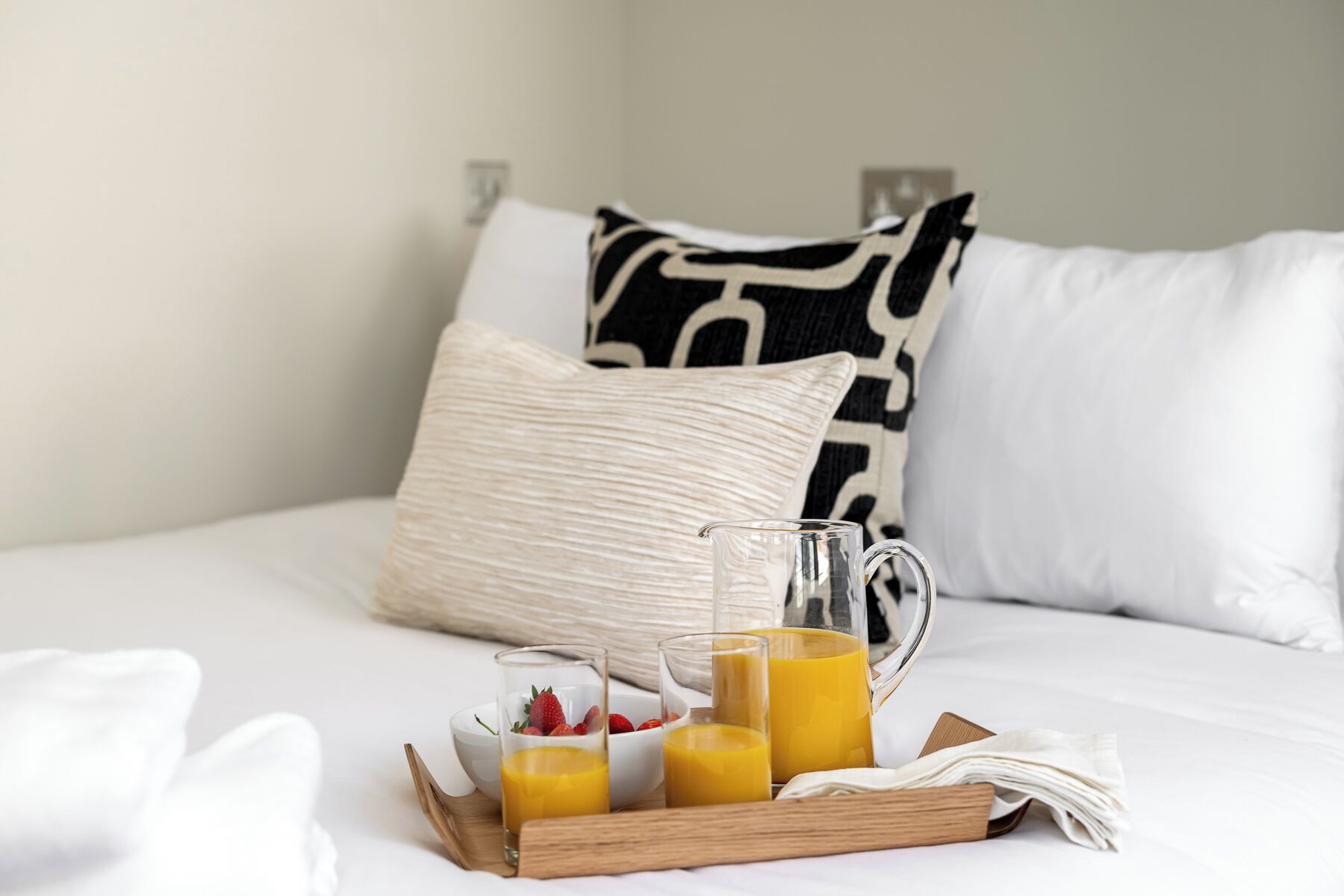 Ein ordentlich gedecktes Frühstücksbuffet mit Orangensaft und Erdbeeren auf einem Bett mit weißen und gemusterten Kissen.