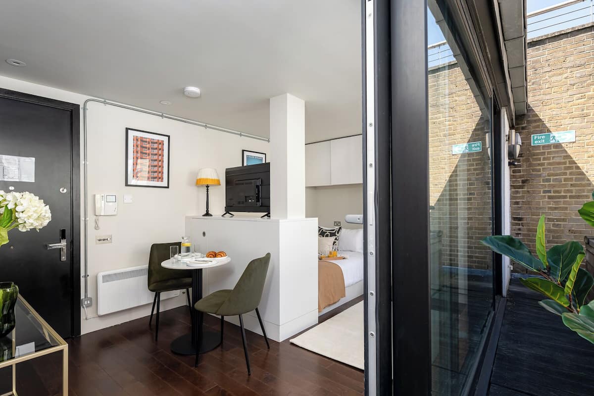 A compact hotel room with a kitchenette, a dining area, a bed, and a view of the outside.