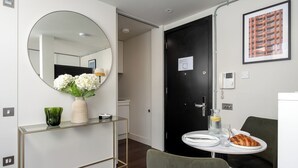 A modern hotel room with a round mirror, a vase of flowers, a small table with a croissant, and a framed picture on the wall. - Your Apartment - Tower of London (London)
