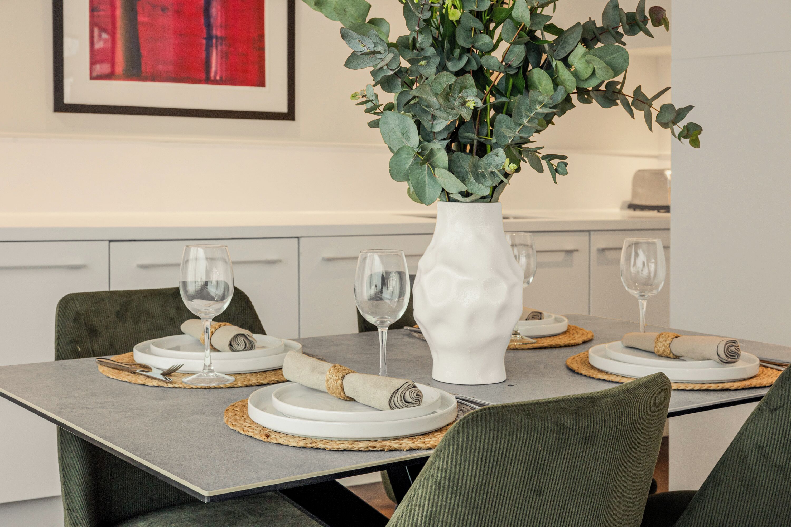 A dining table set with plates, cutlery, and wine glasses, surrounded by upholstered chairs.