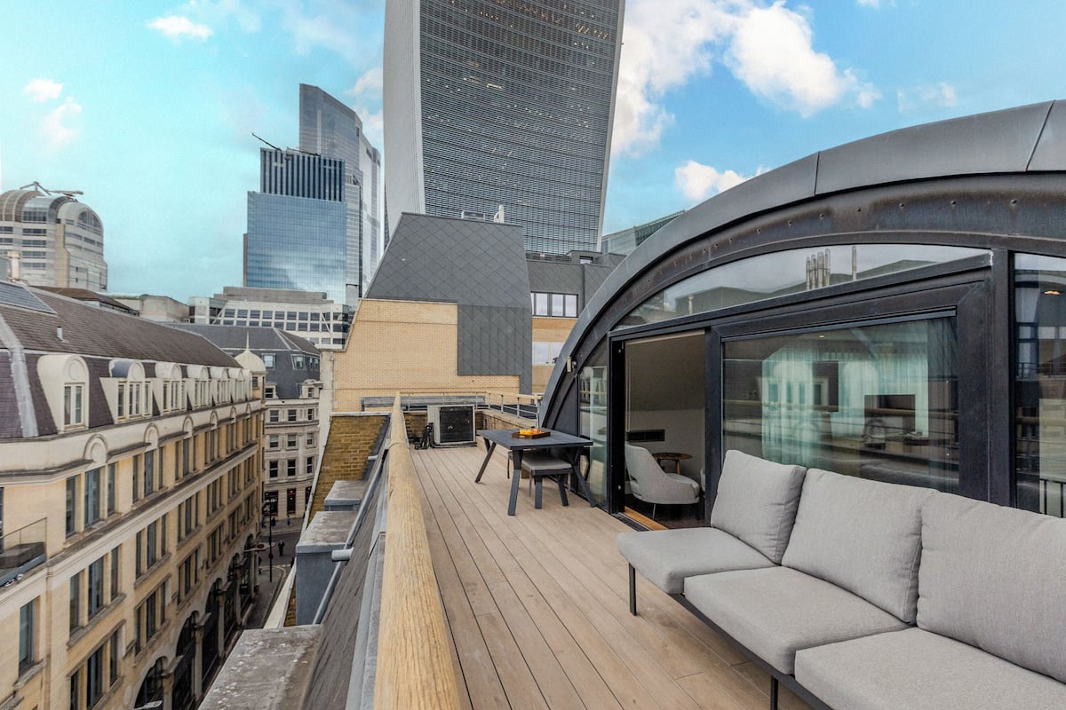 A rooftop terrace with a wooden deck, a sofa, and a table.