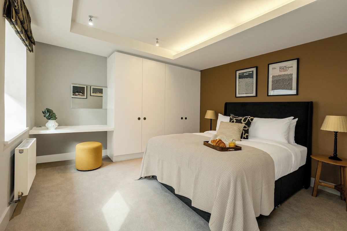 A bedroom with a bed, bedside tables, a bench, a radiator, and framed pictures on the wall.