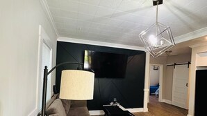 A modern living room with a sectional sofa, a floor lamp, and a flat-screen TV mounted on the wall. - Mimosa house (Goldsboro)