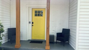 A yellow door with the number 607, a porch with steps, and two black chairs. - Mimosa house (Goldsboro)