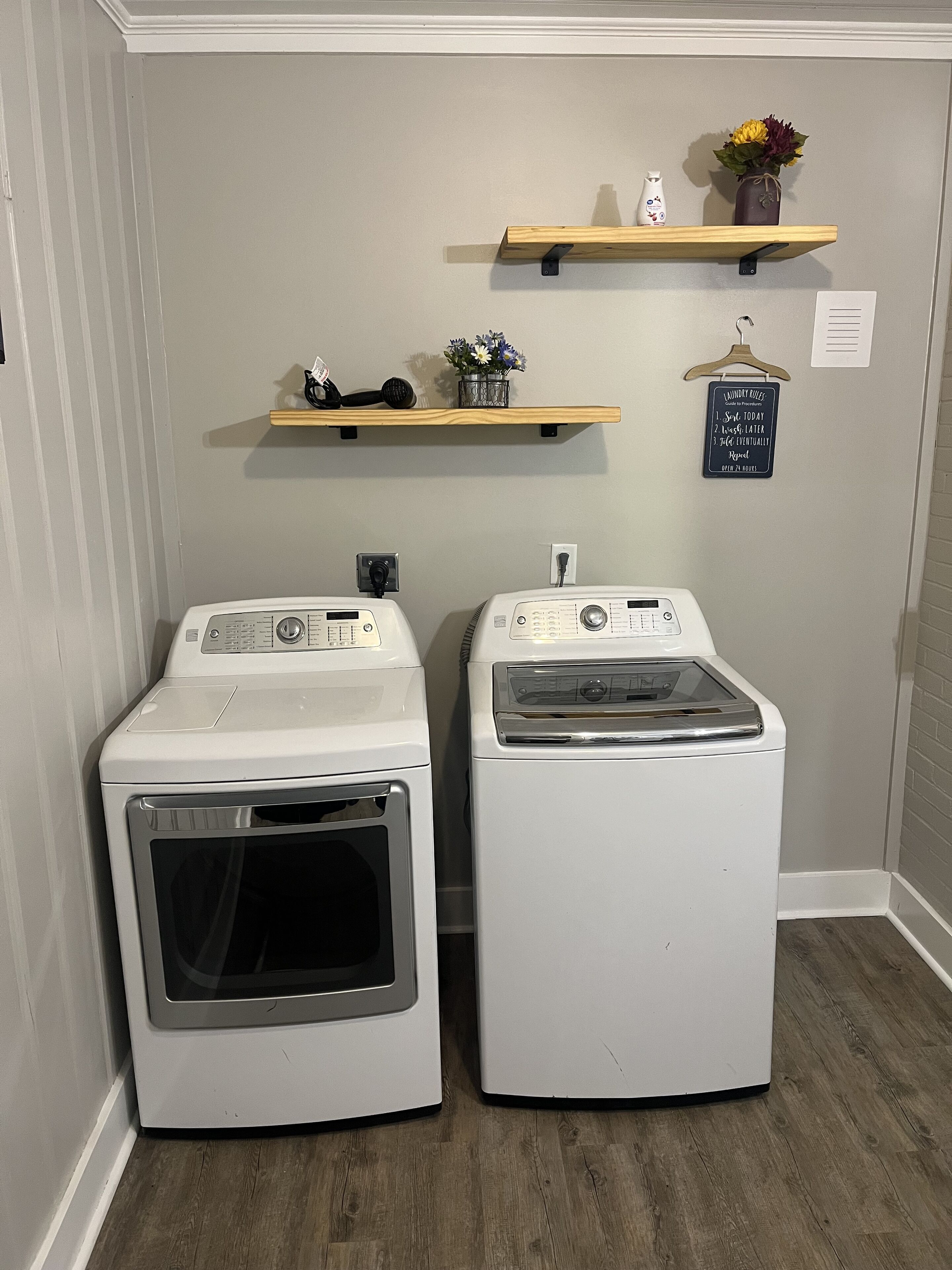 Two front-loading washing machines in a laundry room with wooden shelves above them.