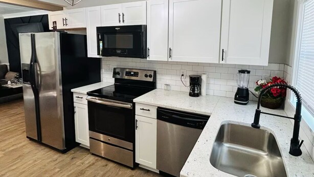 A modern kitchen with stainless steel appliances, white cabinets, and a granite countertop. - Mimosa house (Goldsboro)