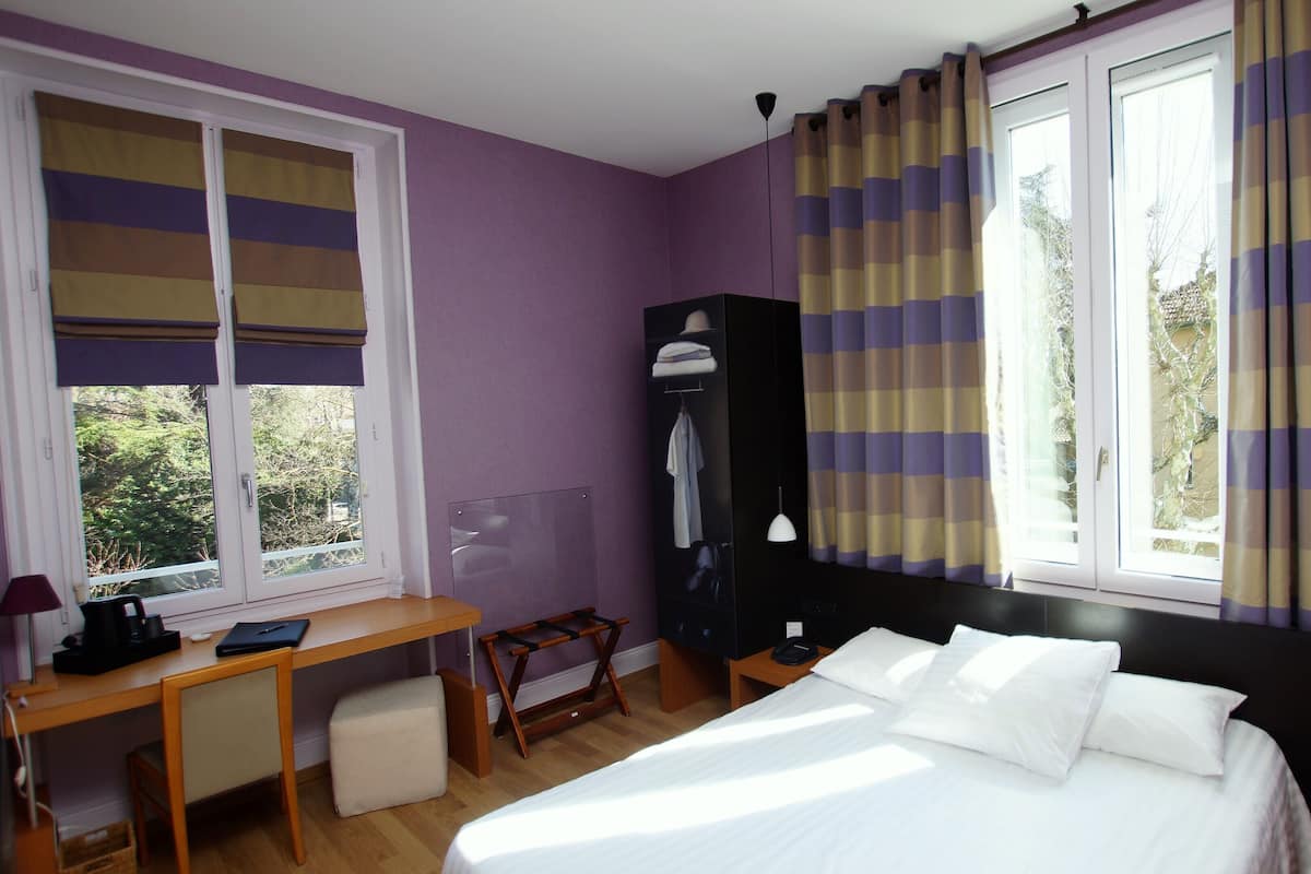 A bedroom with a bed, a desk, a chair, a wardrobe, and a window with curtains.
