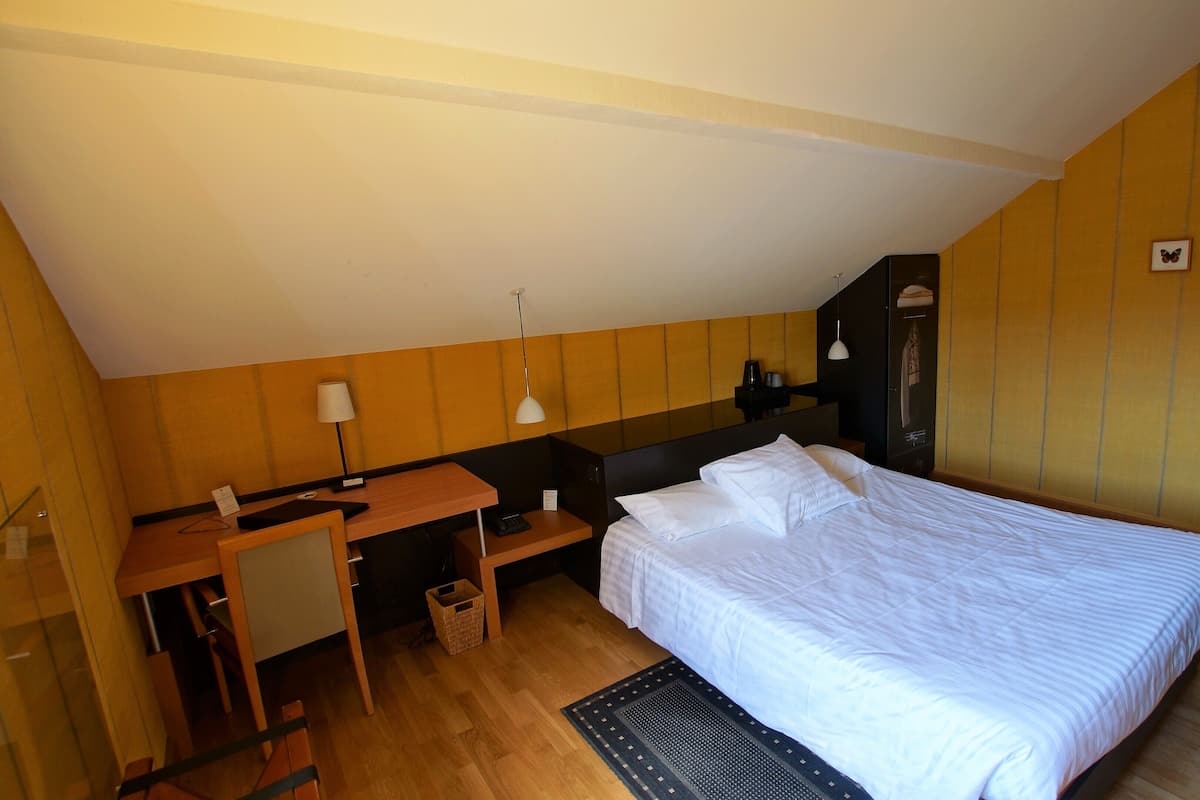 A bedroom with a bed, a desk, a chair, a lamp, and a small table.
