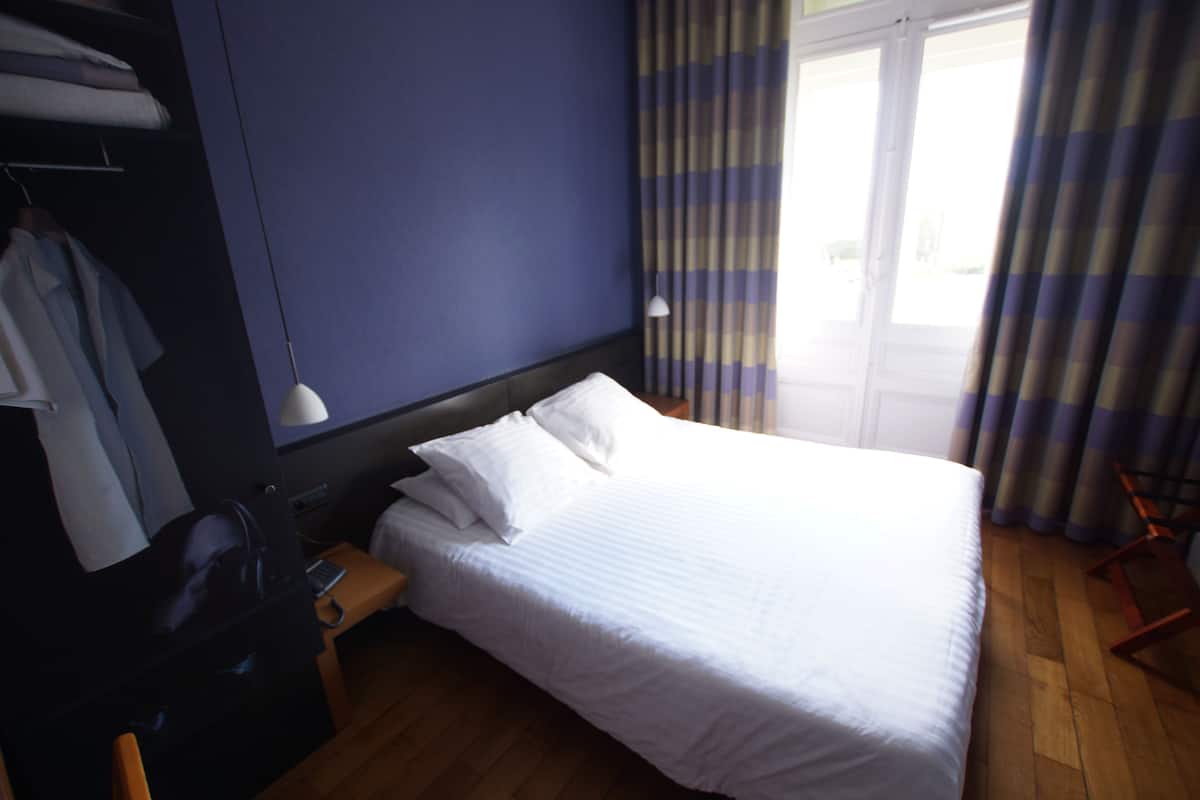 A hotel room with a bed, a desk, a chair, a wardrobe, and a window with curtains.