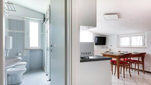 A compact room with a bathroom, a dining area, and a TV. - Three-room flat Apartment Scola 21 (Gabicce Mare)