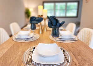 A dining table set with white plates, bowls, and cutlery. - Steps to Lambeau · Garage Lounge · Fire Pit (Ashwaubenon)