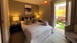 A hotel room with a large bed, two bedside lamps, a painting on the wall, and a view of the outdoor patio through a sliding door.