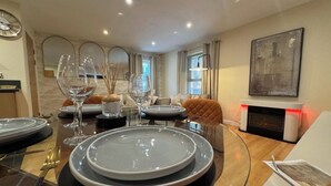 A dining area with a glass table set for four, surrounded by modern decor and a fireplace.