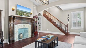 A living room with a fireplace, a staircase, and a large window with blinds.
