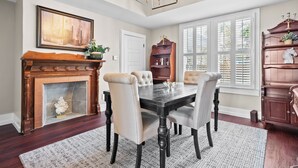 A dining room with a fireplace, a chandelier, and a large window with shutters.